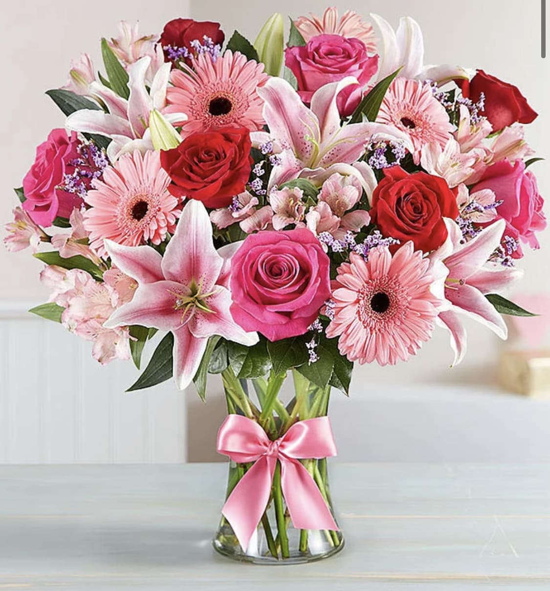 Bouquet of pink and red flowers in a clear glass vase with a pink ribbon