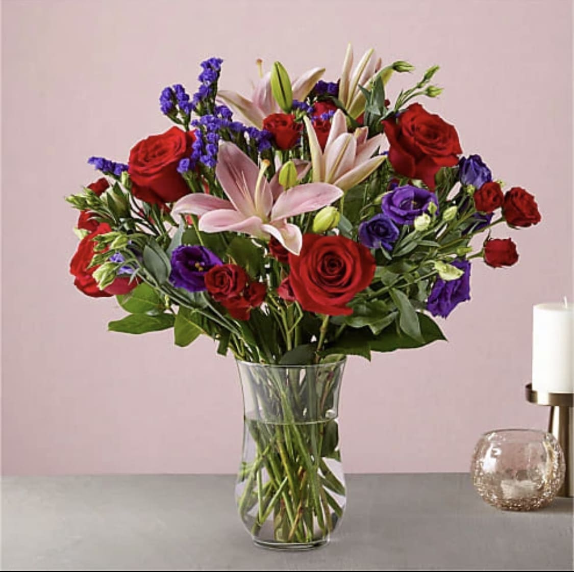 Bouquet of red roses, pink lilies, and purple flowers in a glass vase