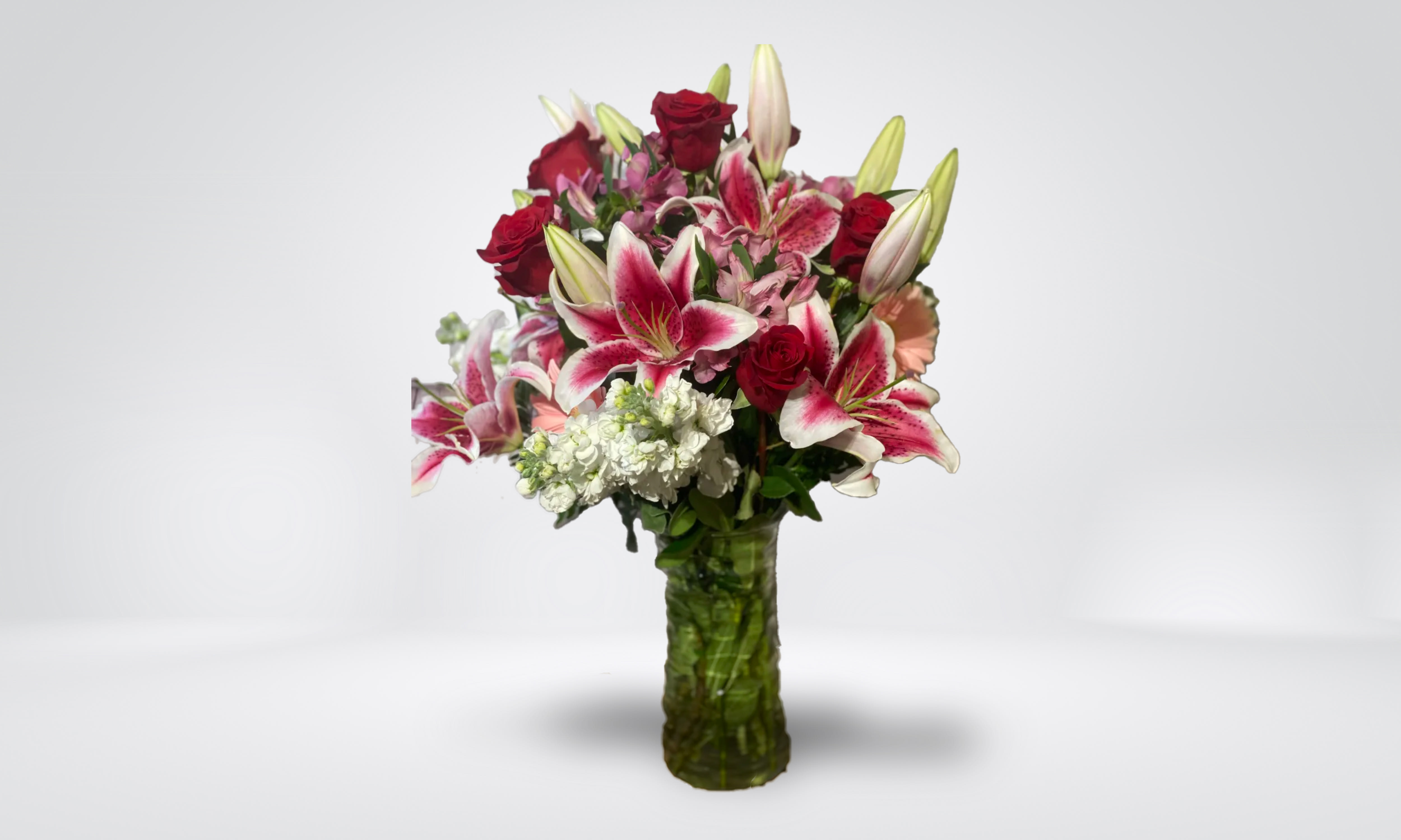 Bouquet of red roses and pink lilies in a green glass vase