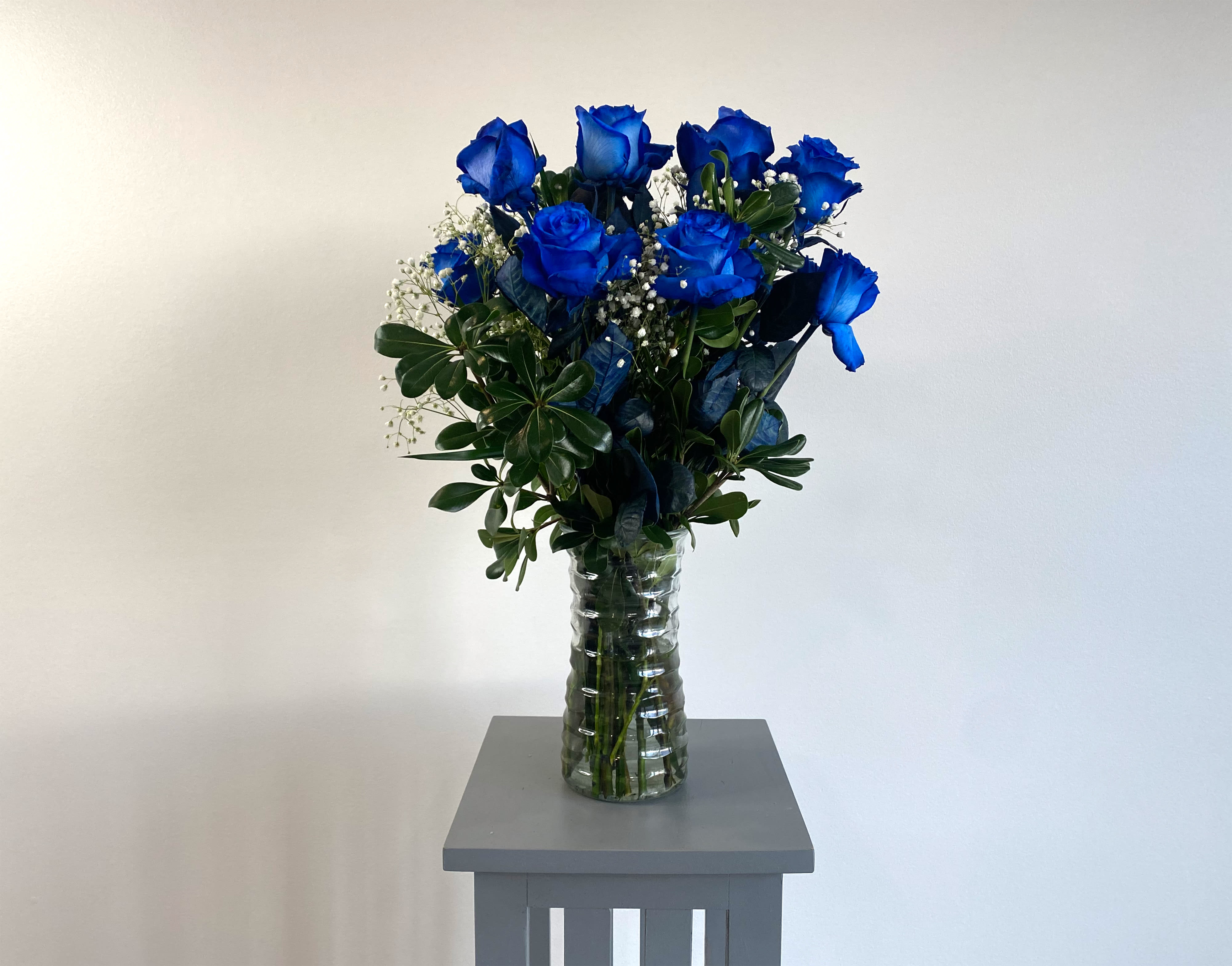 Blue roses in a clear glass vase with greenery