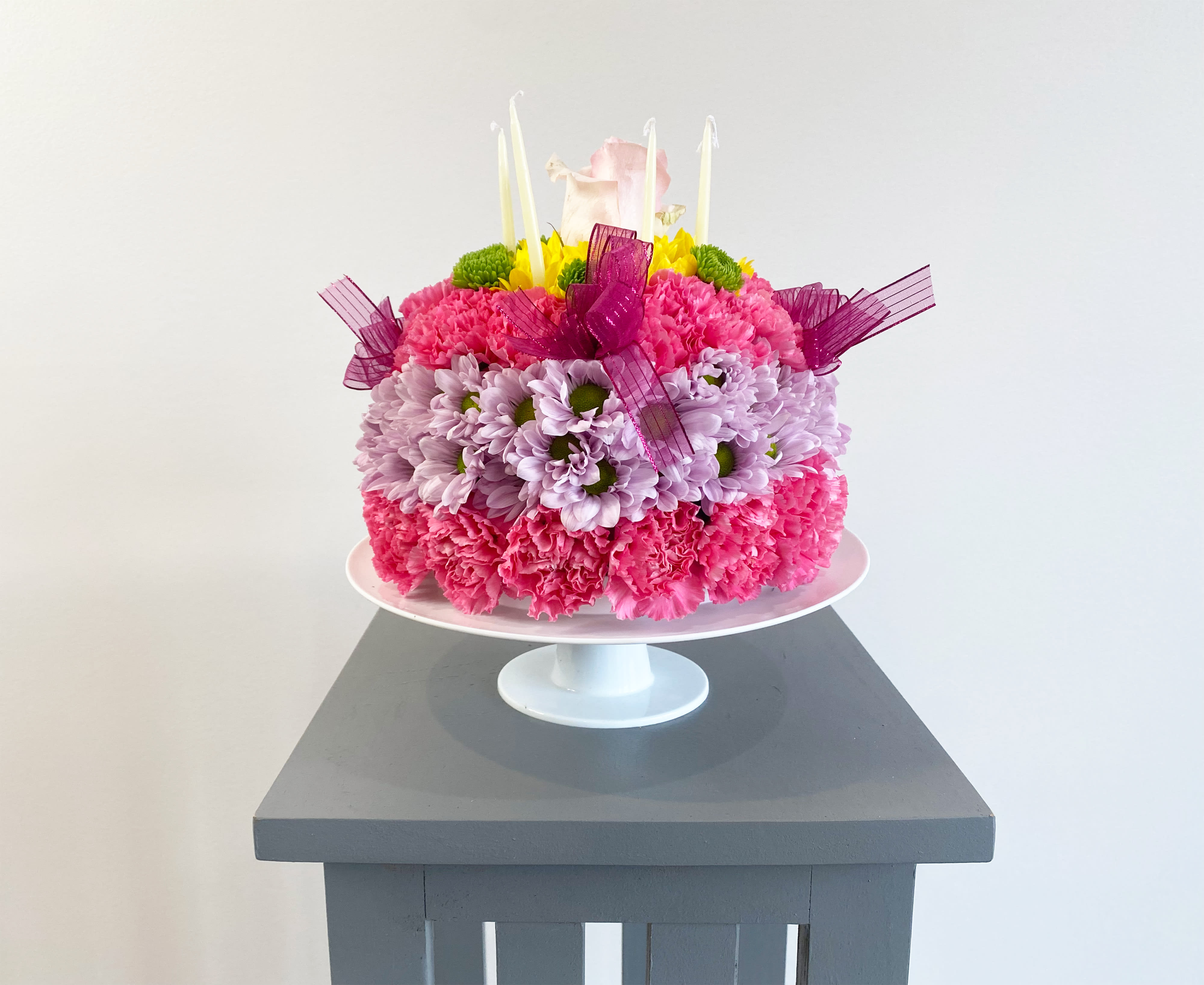 Pink and lavender flower cake with candles on a white pedestal stand