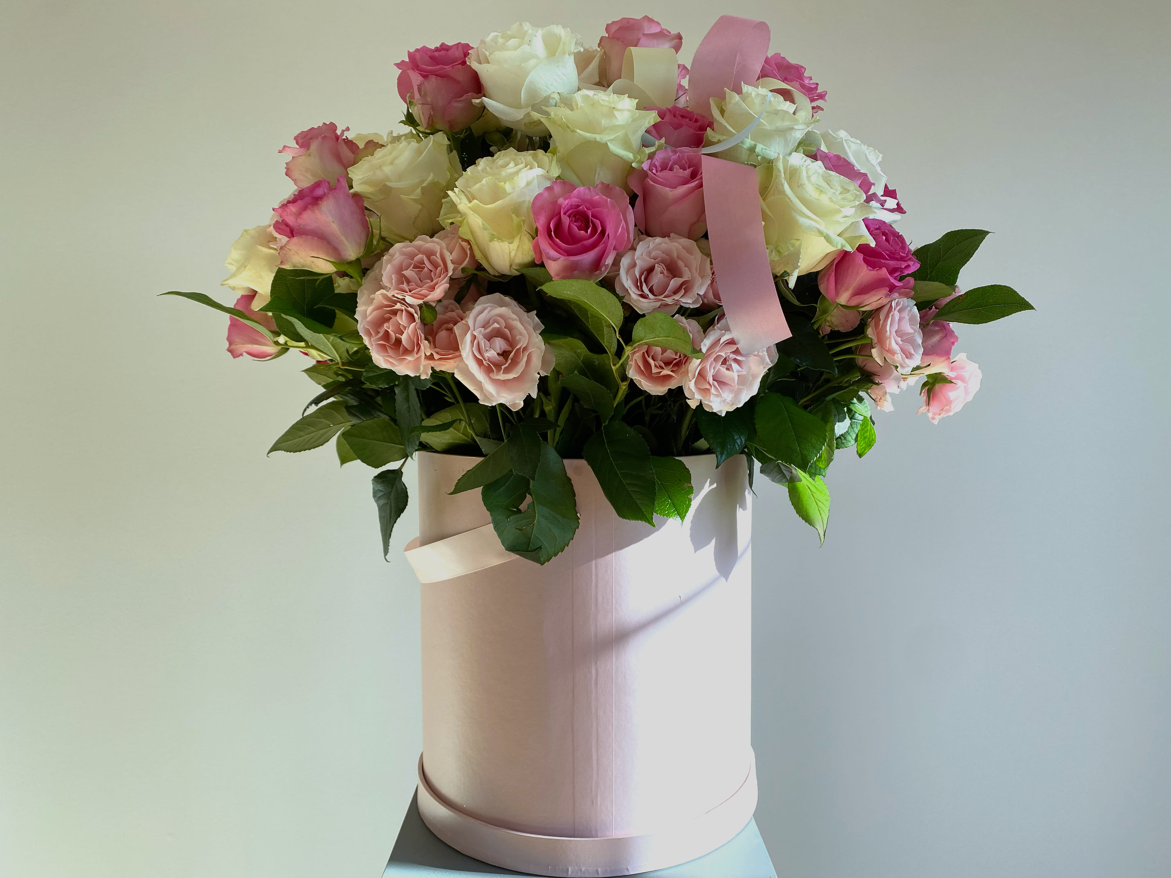 Pink and white roses arranged in a round hatbox with ribbon