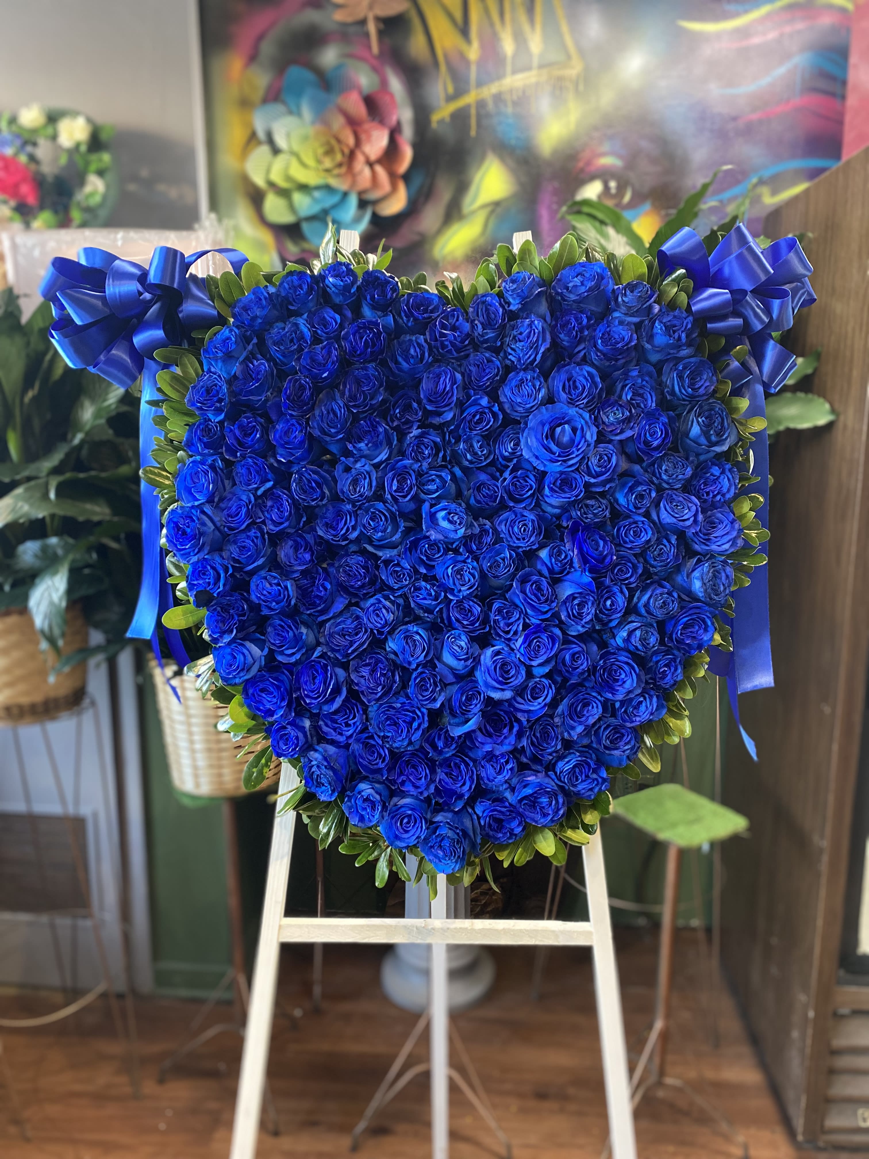 Heart-shaped arrangement of blue roses with ribbon bows on an easel