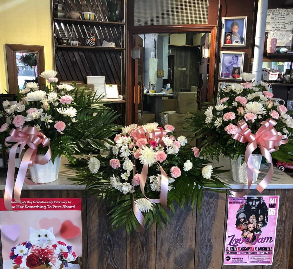 Three pink and white floral arrangements with ribbons in white containers