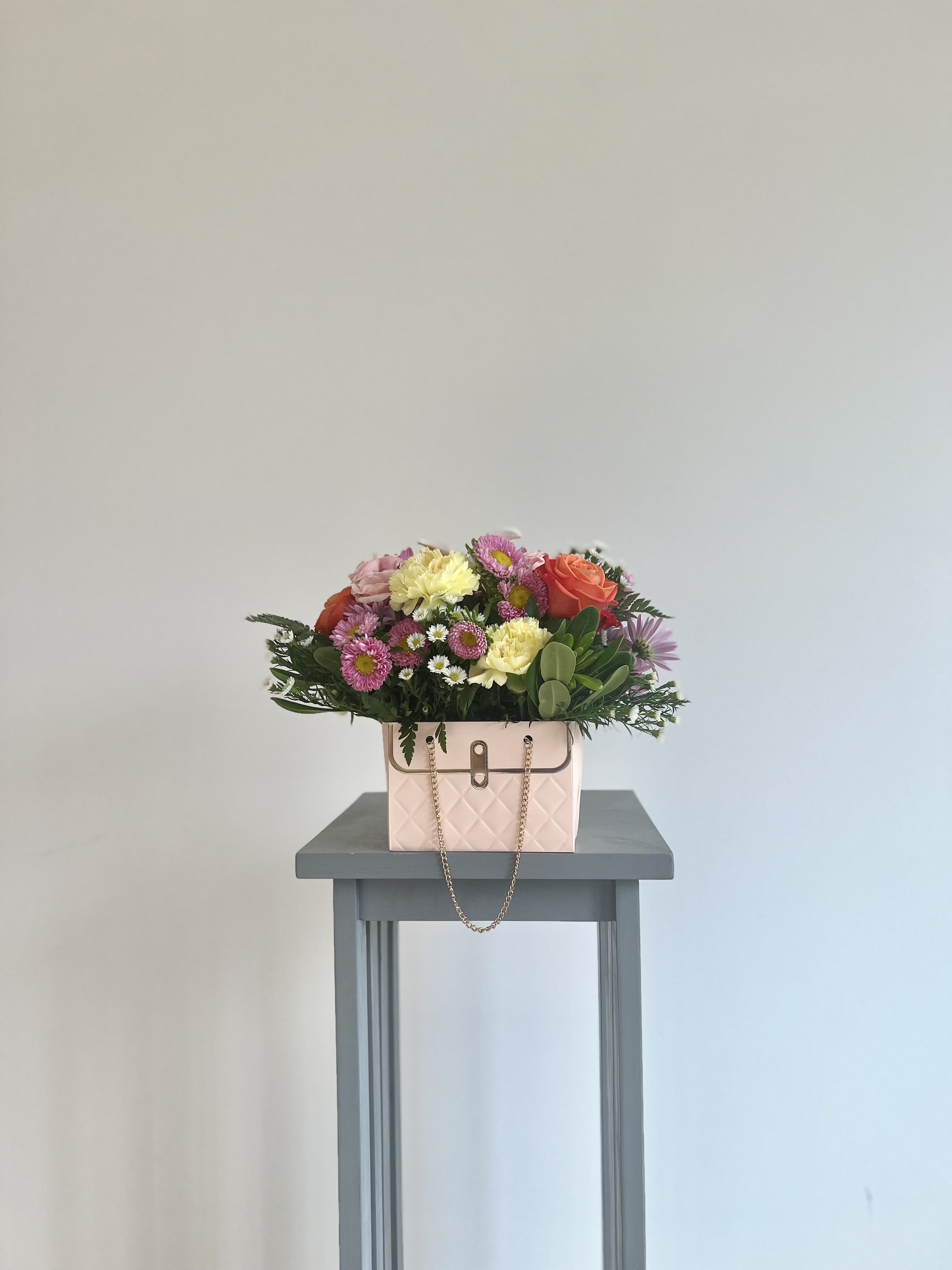 Mixed bouquet in a pink handbag-style container on a small table