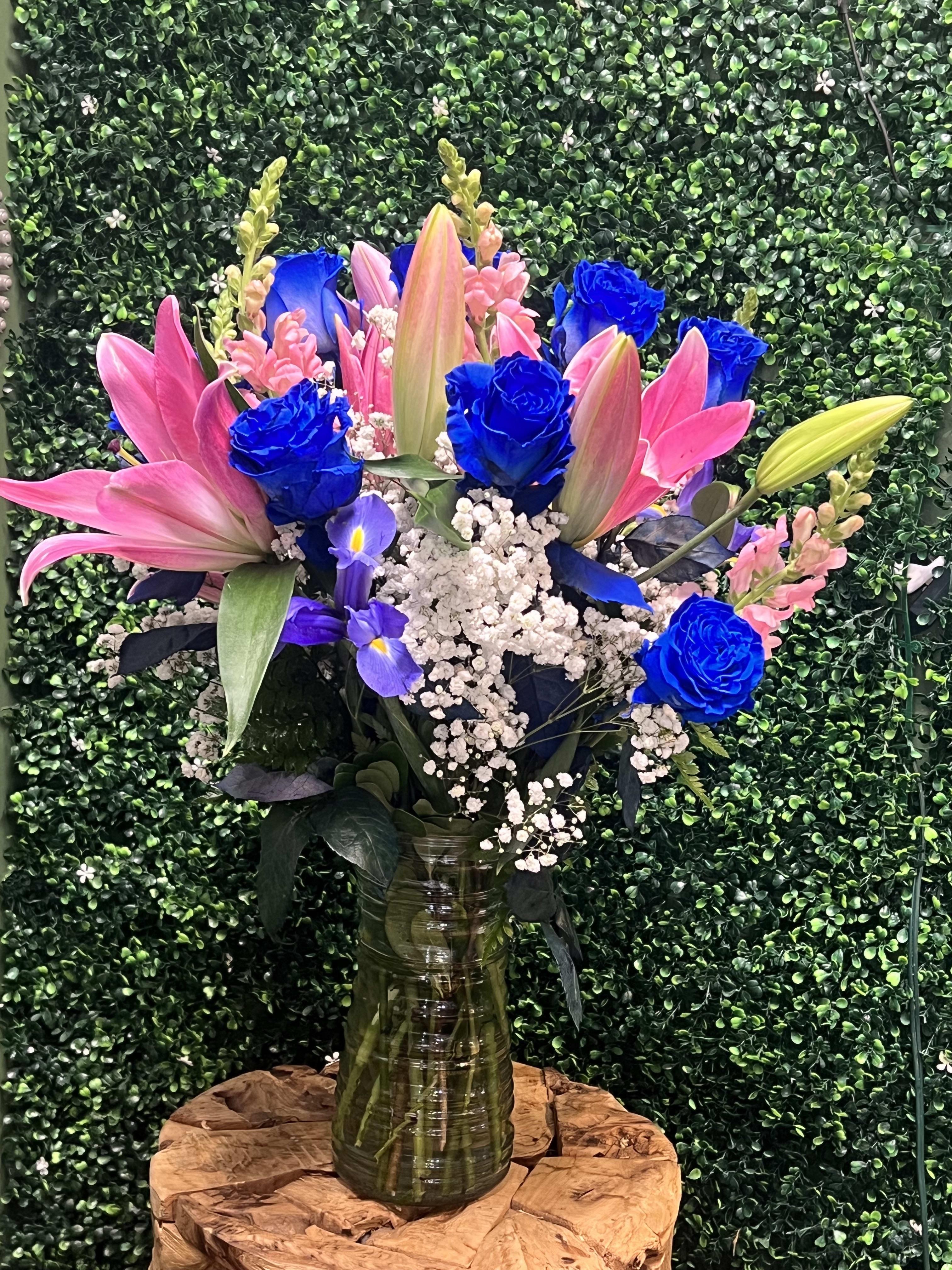 Bouquet of pink lilies, blue roses, and white baby's breath in a glass vase