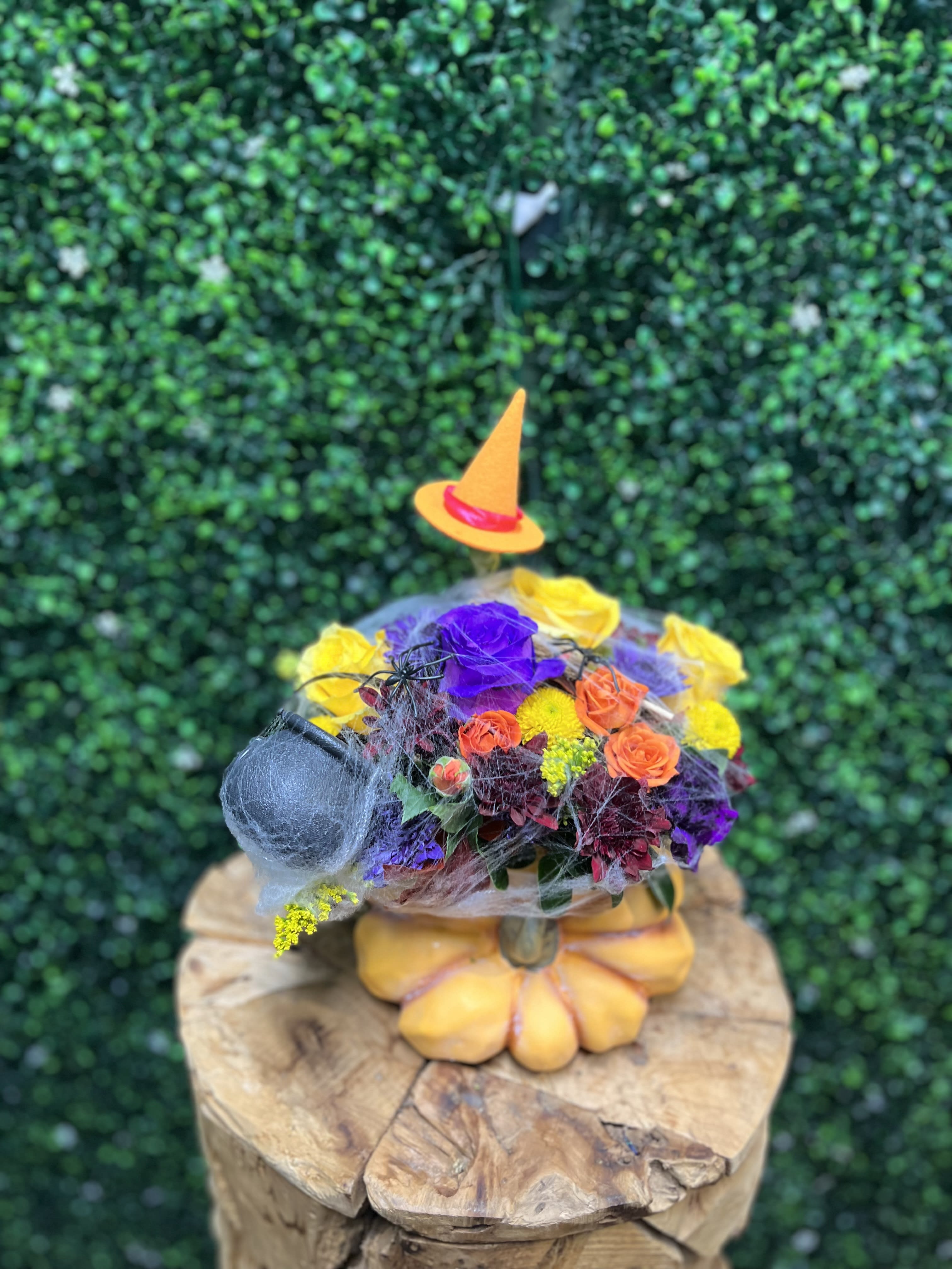 Colorful floral arrangement in a pumpkin-shaped container with a small witch hat
