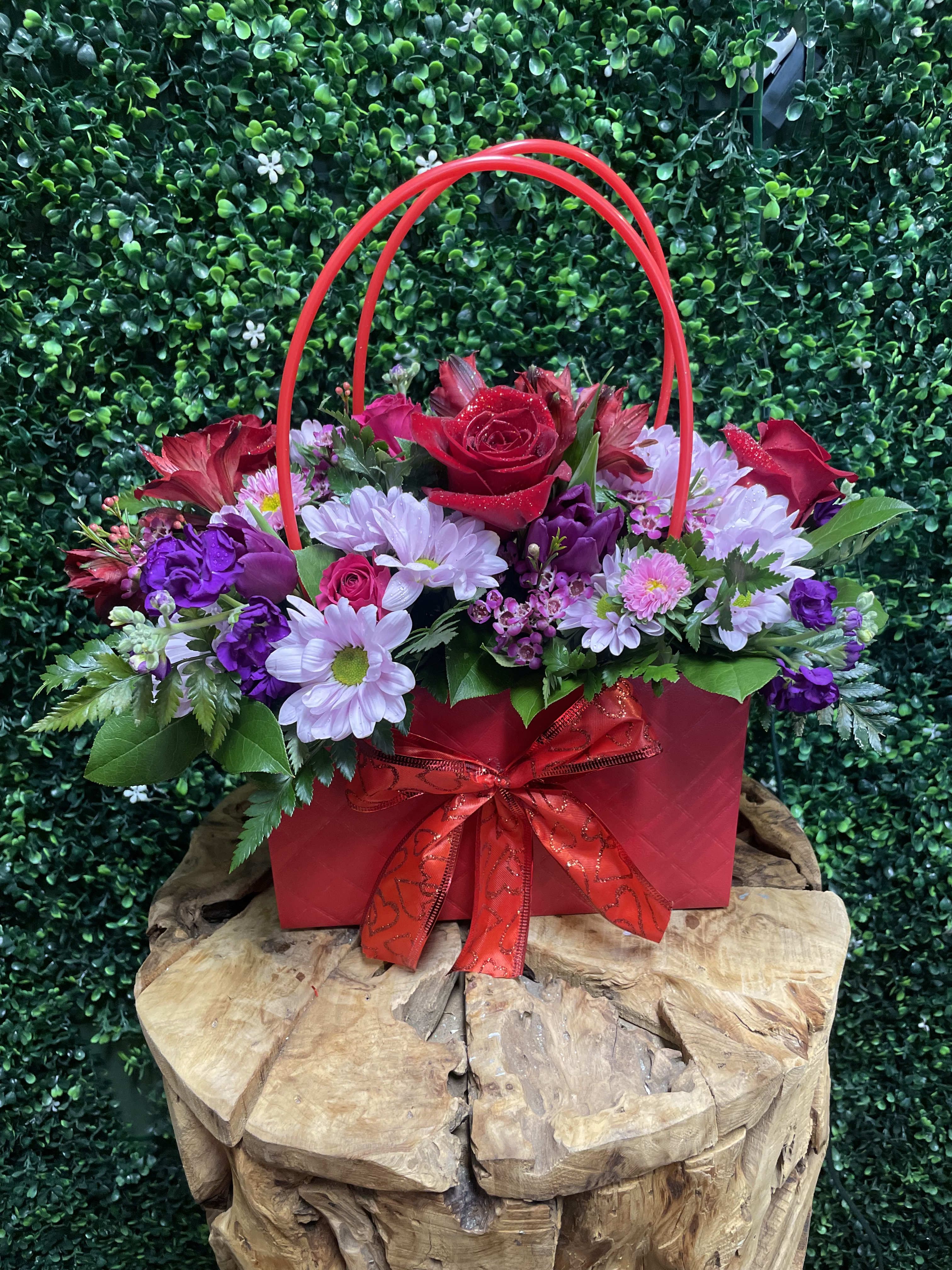 Red and purple flower arrangement in a red gift bag with ribbon