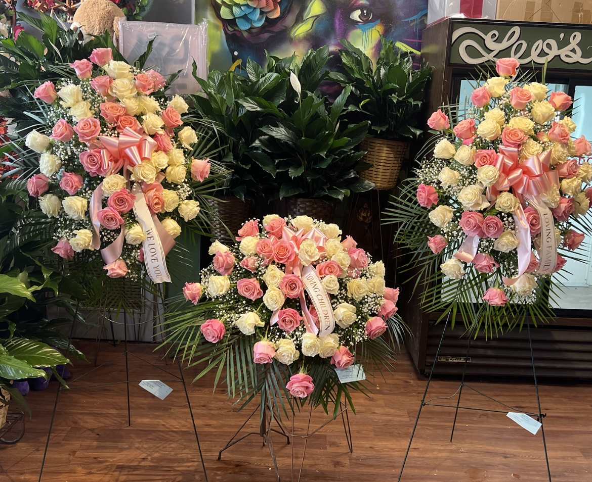 Three standing rose wreaths with pink and cream blooms and ribbons