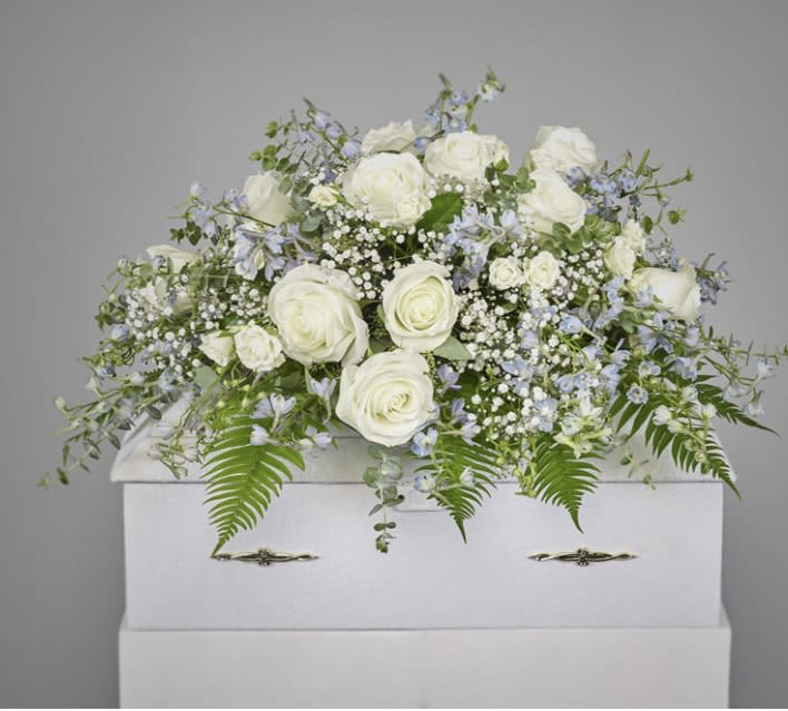 White roses and pale blue flowers arranged on a white casket