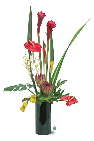 Tall tropical arrangement in a dark vase with red blooms and long green leaves