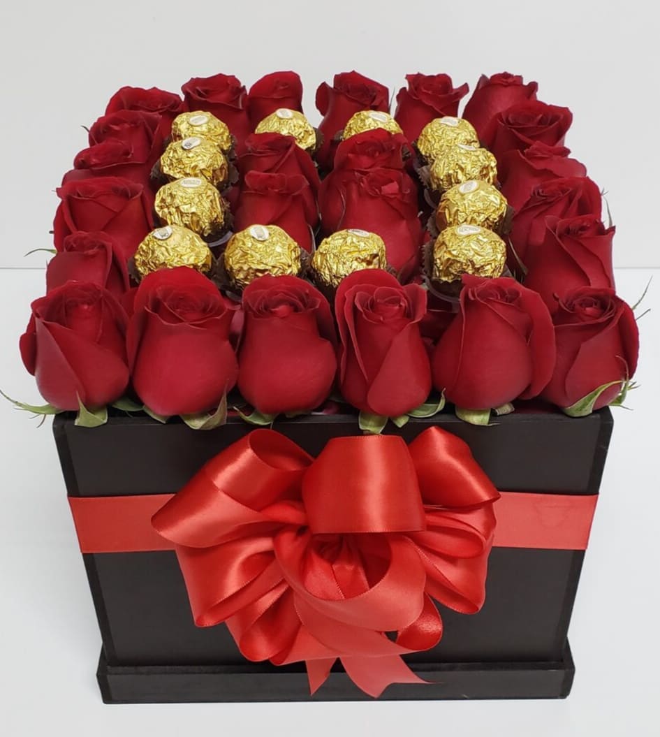 Red roses and gold-wrapped chocolates arranged in a black gift box with a red bow.