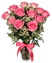 Pink roses arranged in a glass vase with a pink ribbon