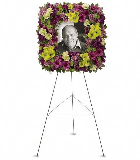 T269-1A  Mosaic of Memories Square Easel Wreath - A unique and lovely tribute for the service, this contemporary square easel wreath of purple and green flowers is a gift of caring expressed with beauty and style. The elegant arrangement includes purple alstroemeria, green gladioli, green carnations, purple cushion spray chrysanthemums, lavender button spray chrysanthemums, green button spray chrysanthemums and purple button spray chrysanthemums, accented with assorted greenery. Approximately 23 1/2" W x 23 1/2" H 