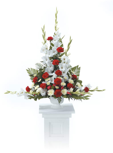 Tall red and white floral spray in a white pedestal vase