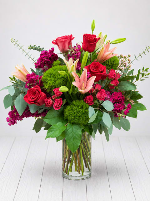Bouquet of red roses, pink lilies, and purple flowers in a glass vase