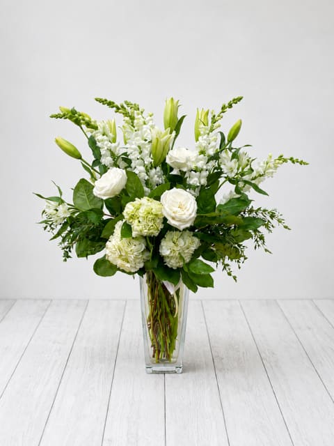 White flowers arranged in a clear glass vase with green accents