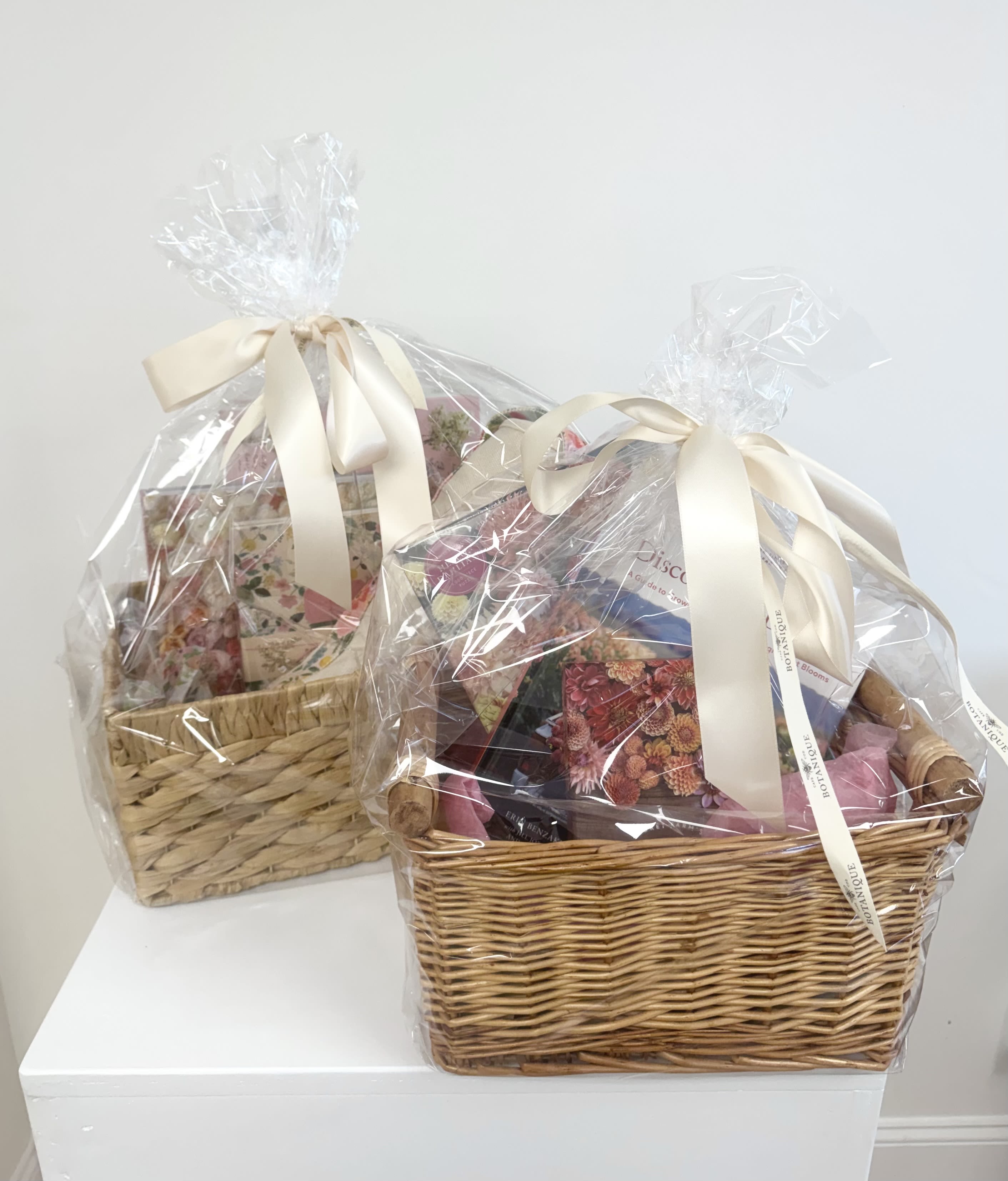 Two wrapped gift baskets with ribbon bows on a white surface