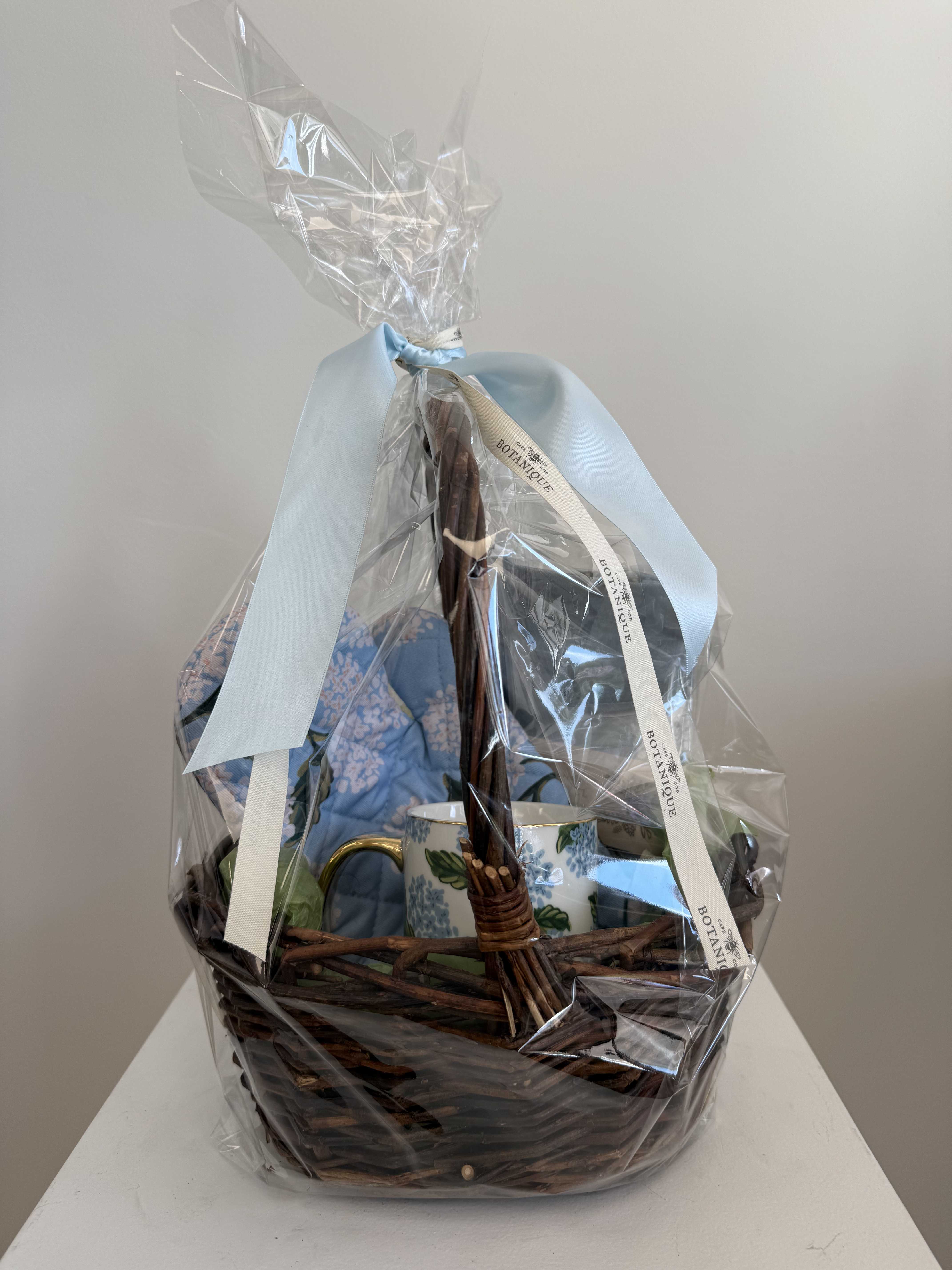 Gift basket with a blue mug and wrapped items in a wicker basket
