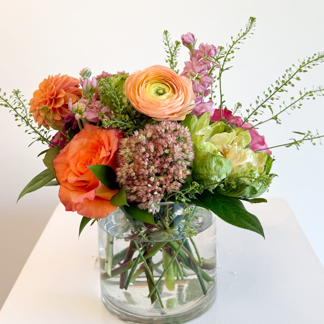 Mixed bouquet of orange, pink, and peach flowers in a clear glass vase