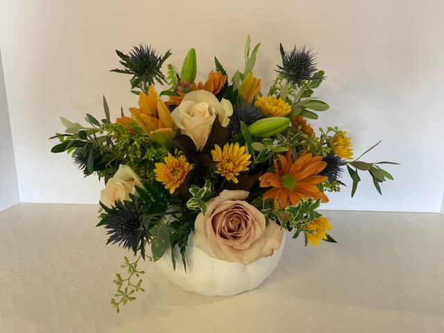 Mixed bouquet in a white pumpkin-shaped vase with cream roses and orange blooms
