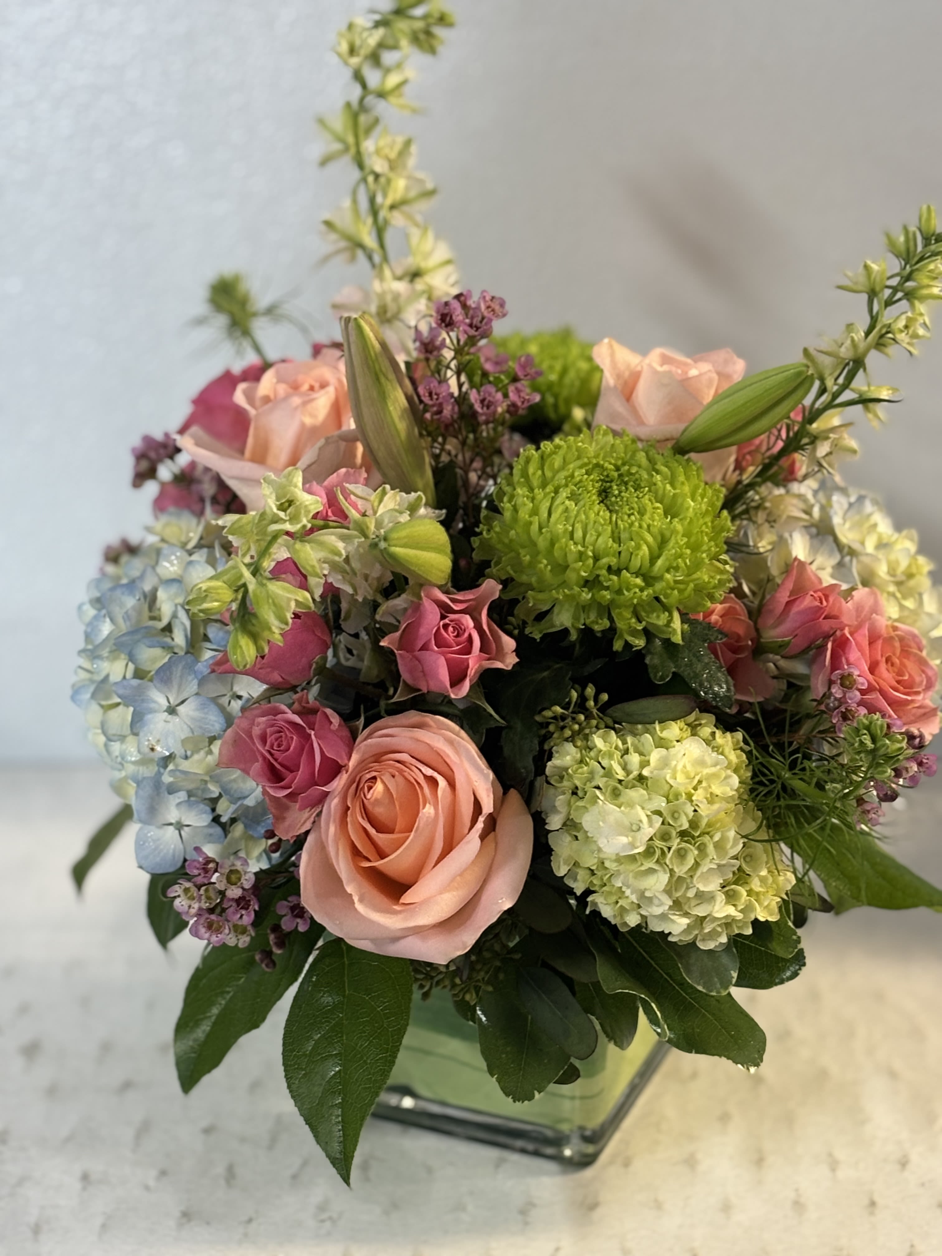 Mixed bouquet of pink roses, hydrangeas, and green chrysanthemums in a glass vase