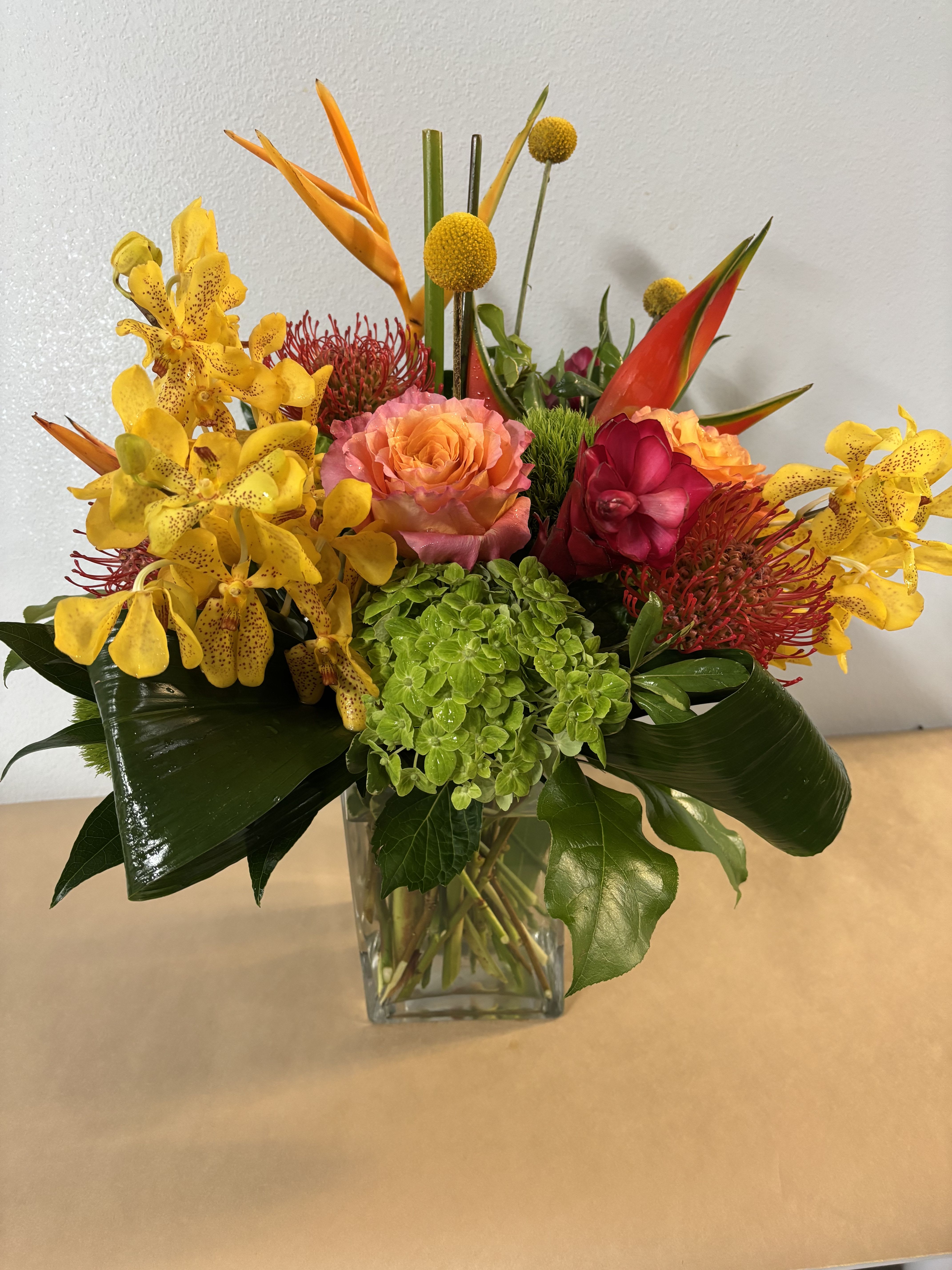 Tropical bouquet in a clear glass vase with yellow orchids and orange-red blooms