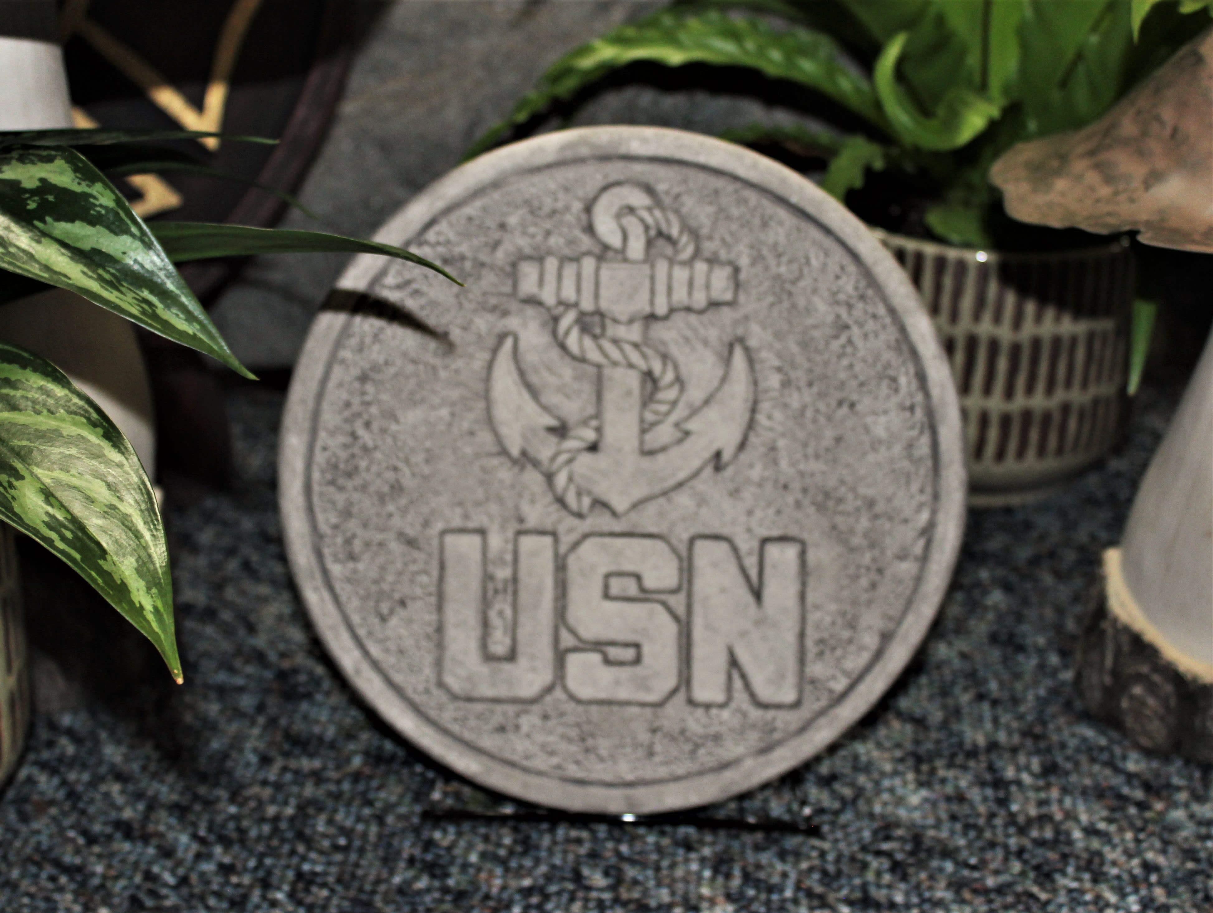 Round stone plaque with a USN anchor emblem surrounded by potted plants