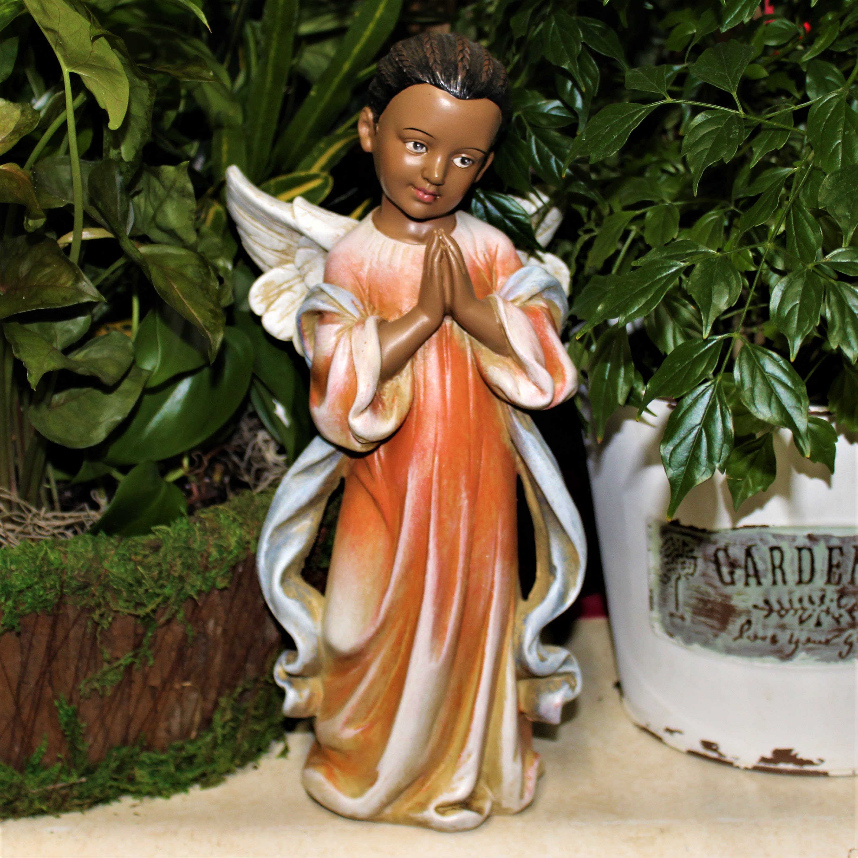 Angel figurine in an orange and white robe surrounded by potted greenery