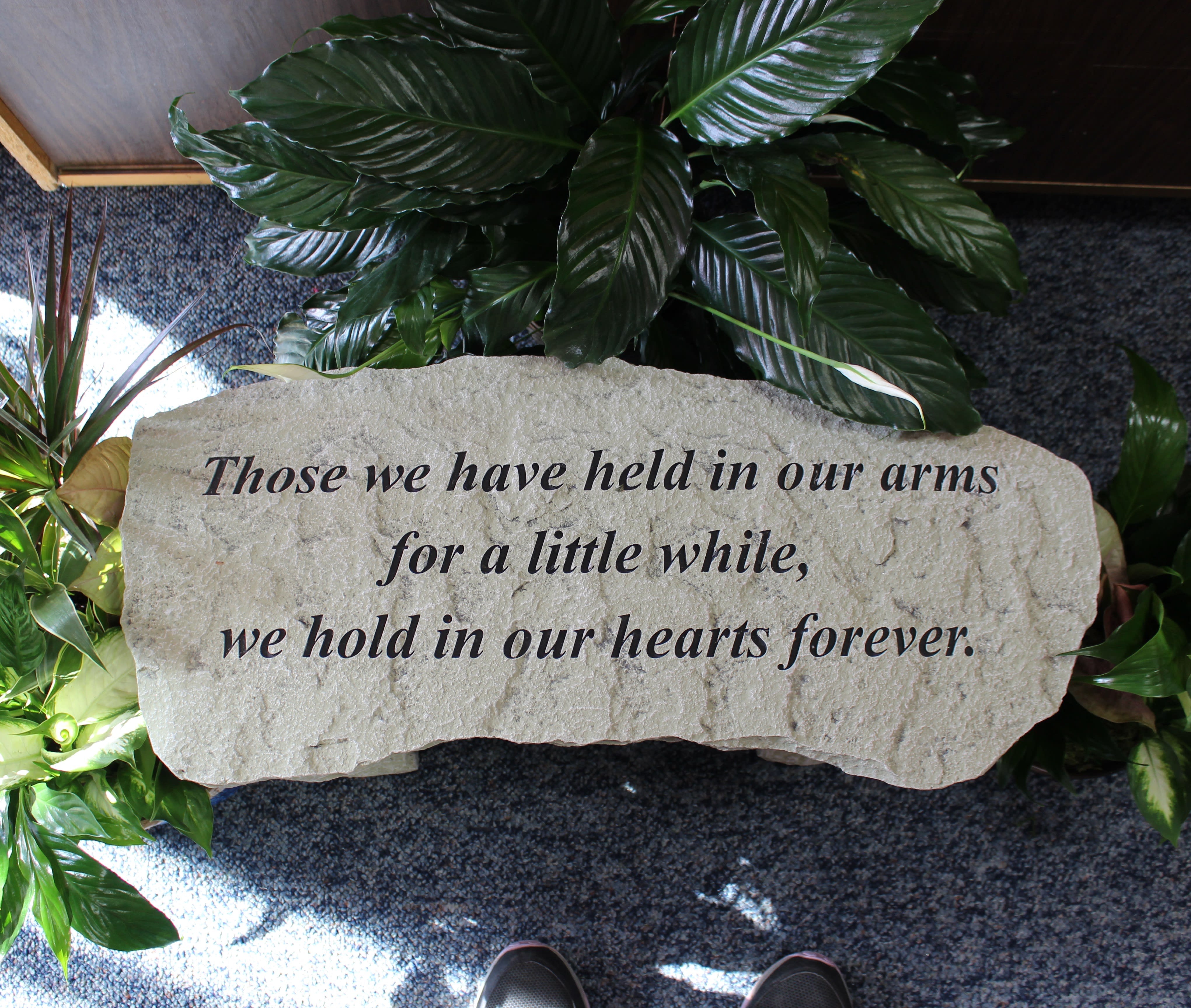 Memorial stone with engraved sympathy message surrounded by green plants