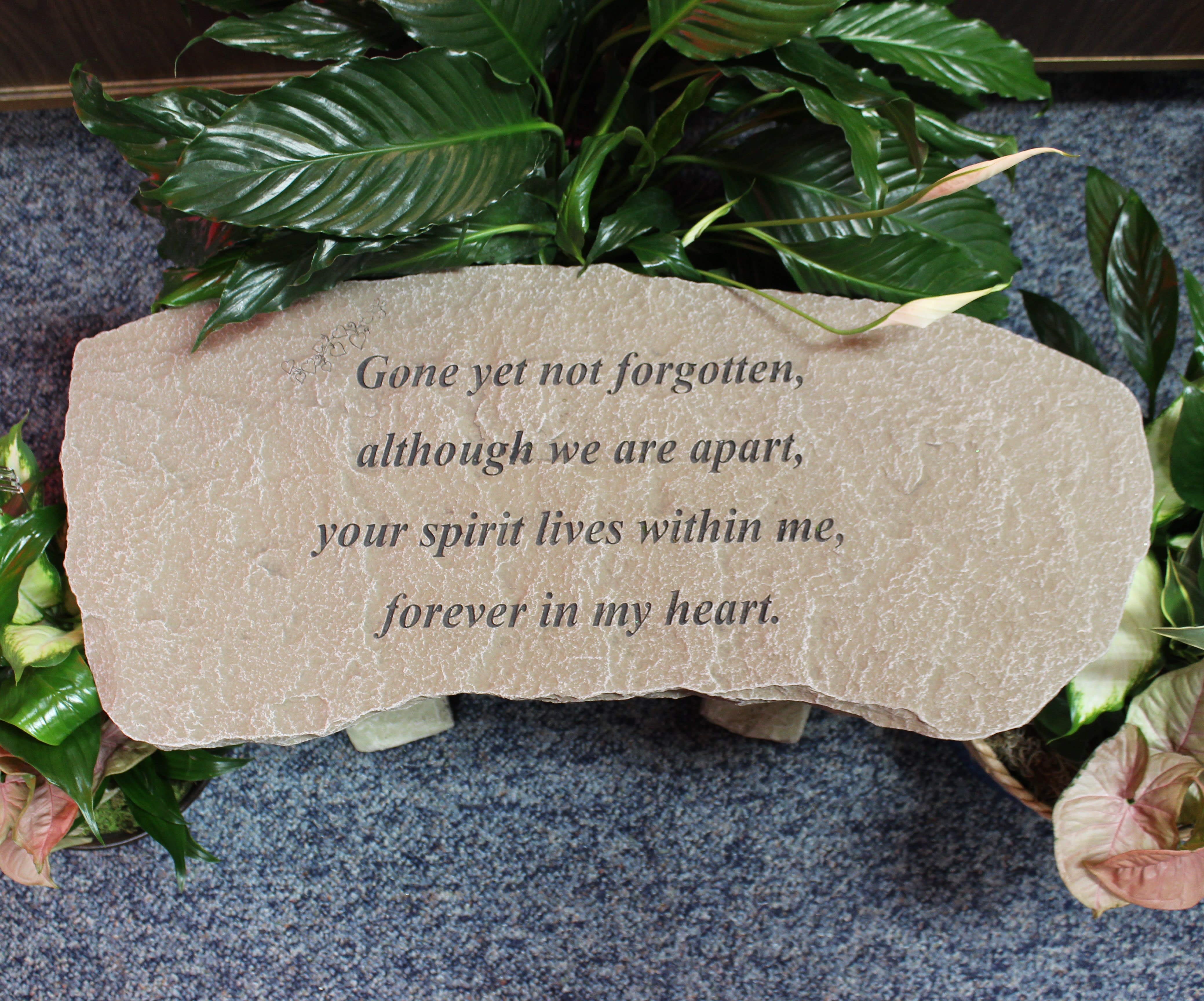 Memorial stone with engraved text surrounded by green plants