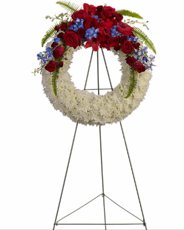 Standing floral wreath with red roses, white flowers, and blue accents on an easel