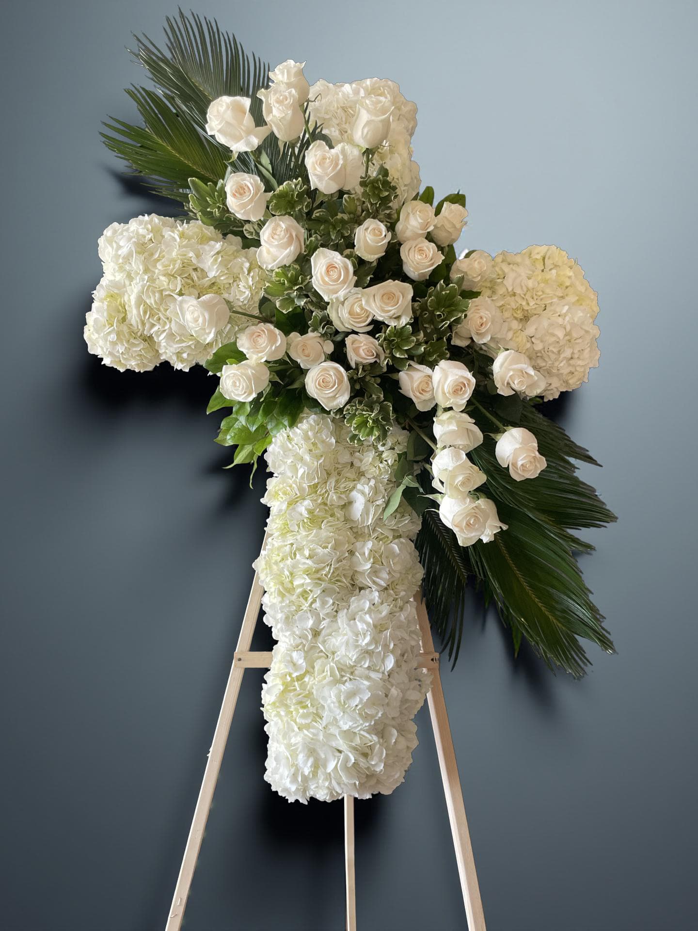 White floral cross on an easel with roses and hydrangeas