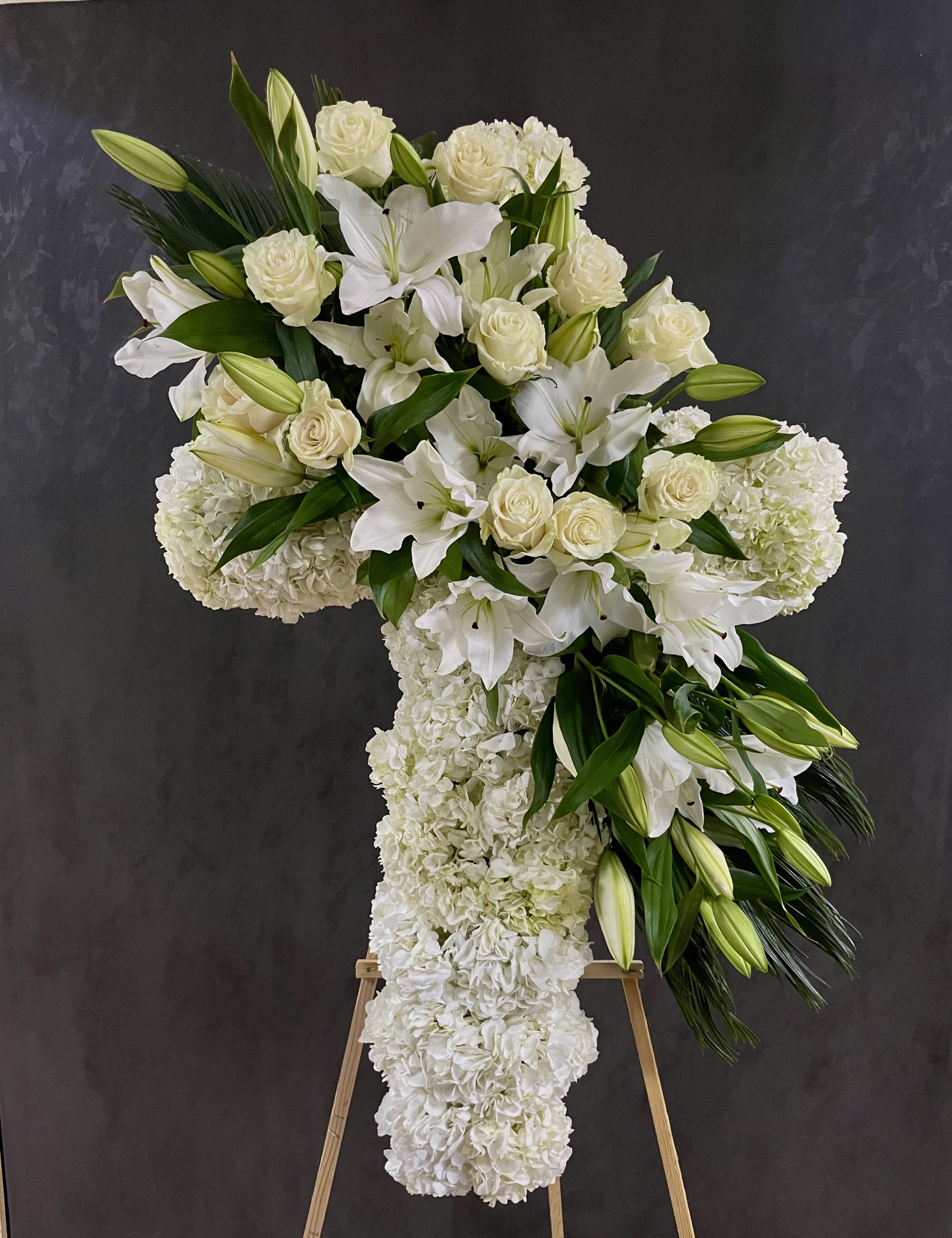 White floral cross arrangement on an easel with lilies and roses