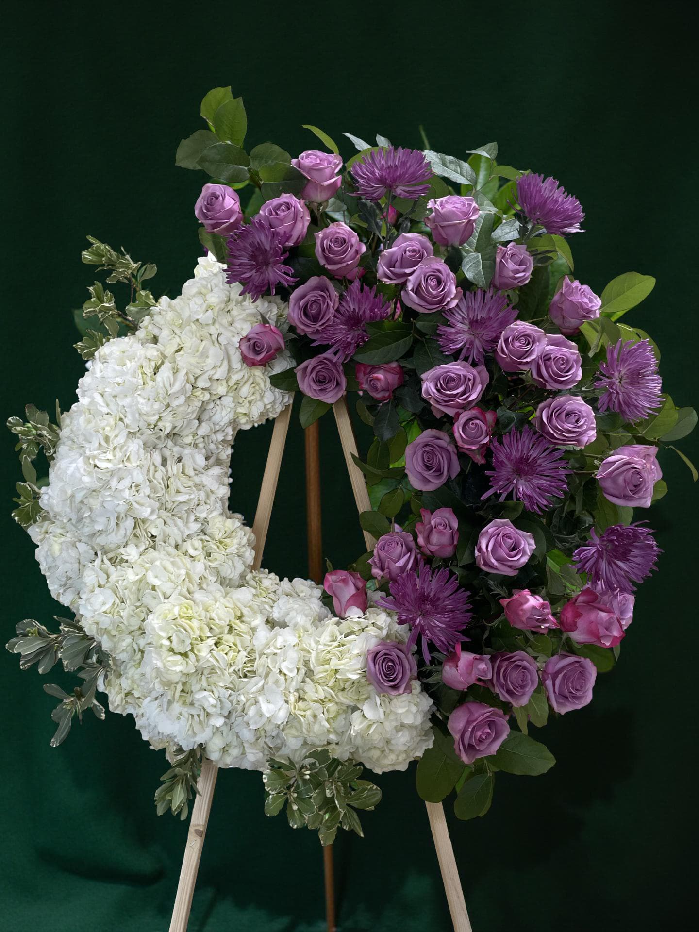 Floral wreath with white hydrangeas, purple roses, and purple mums on an easel