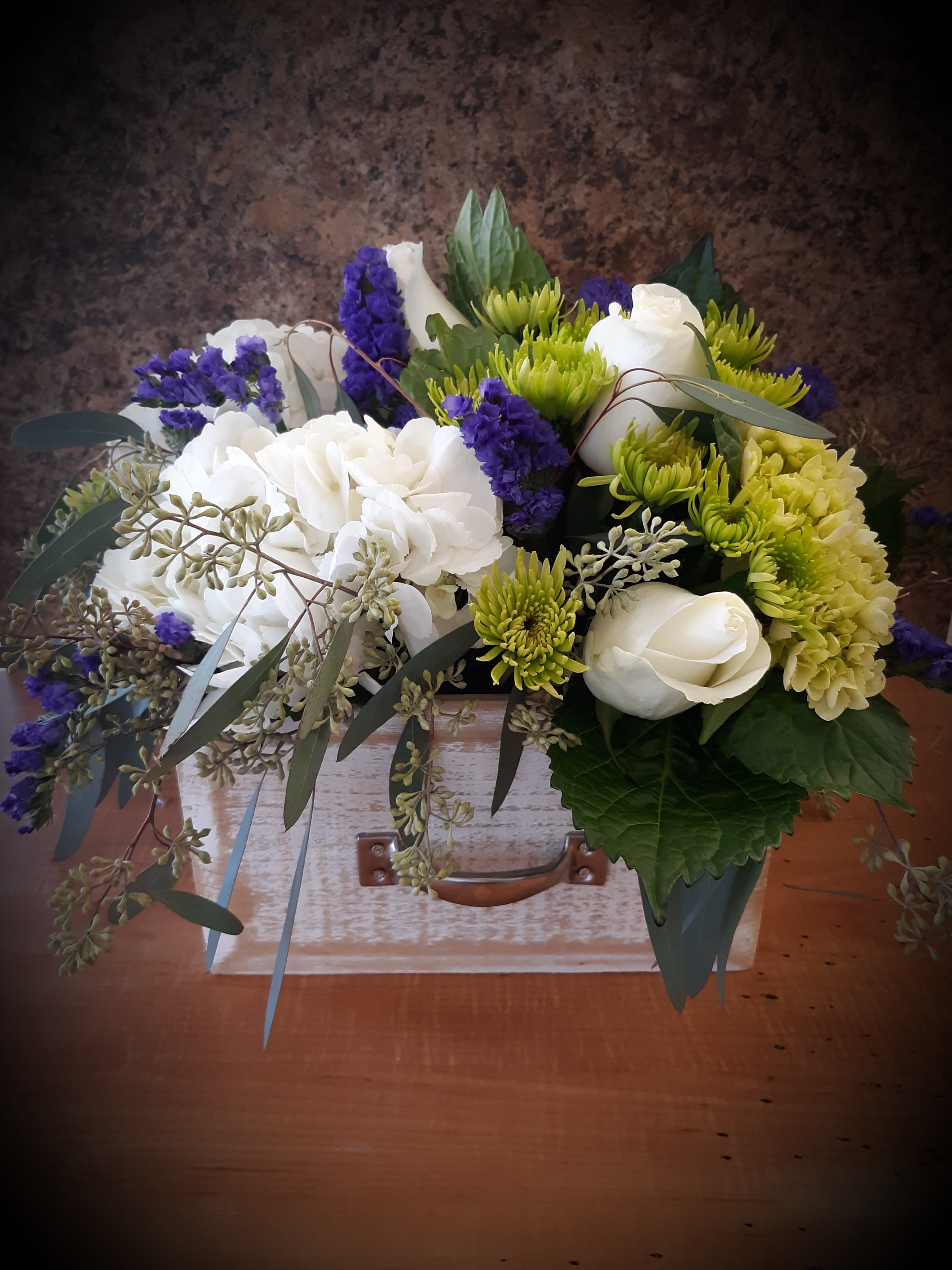 Bouquet of white roses, green chrysanthemums, and purple filler flowers in a wooden box