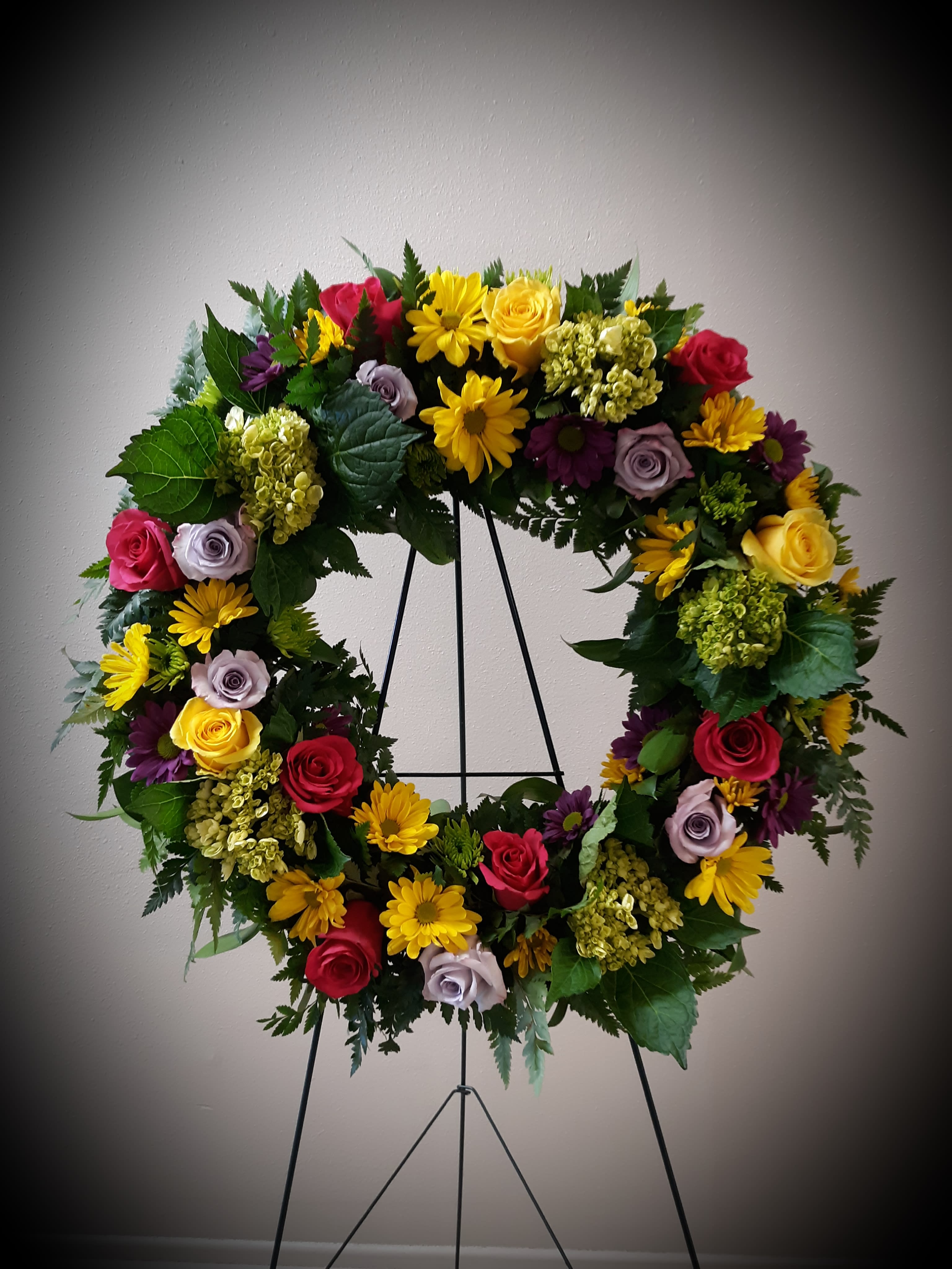Colorful floral wreath on a black stand with roses and daisies