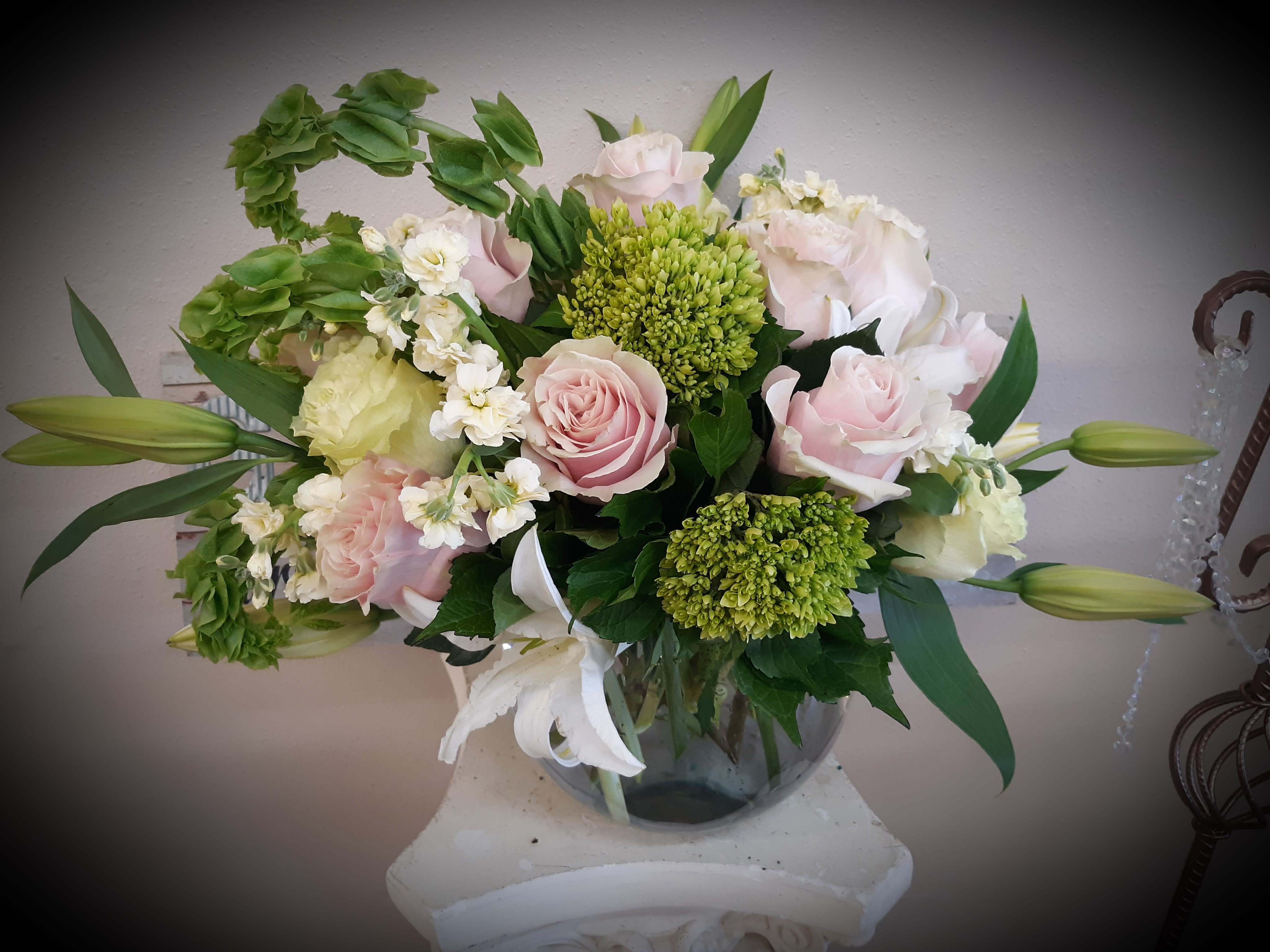 Pink and white roses arranged in a glass vase with green blooms