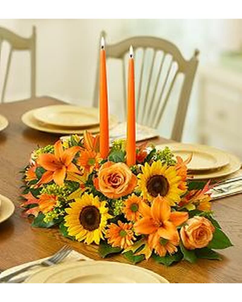 Orange floral centerpiece with two tall taper candles on a dining table