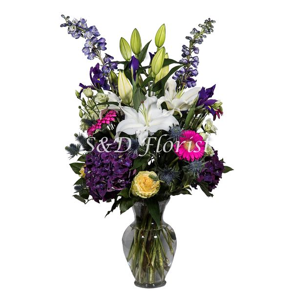 Mixed bouquet of lilies, roses, hydrangeas, and purple flowers in a glass vase