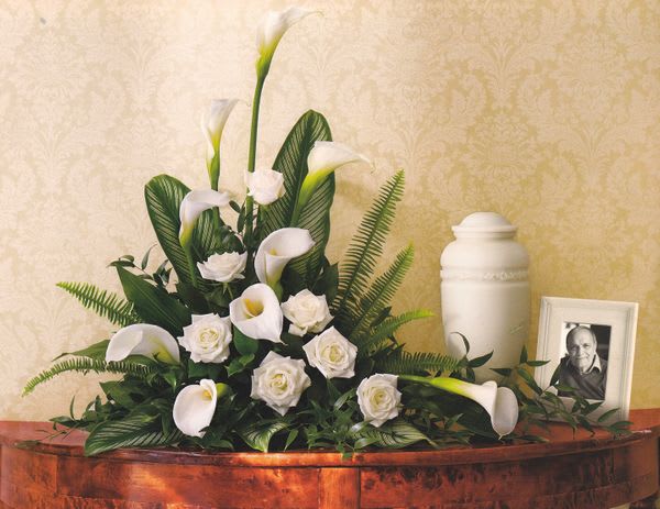White calla lilies and roses arranged beside an urn and framed photo