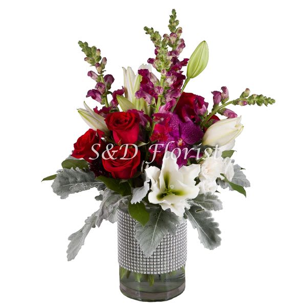Bouquet of red roses, white lilies, and purple snapdragons in a glass vase
