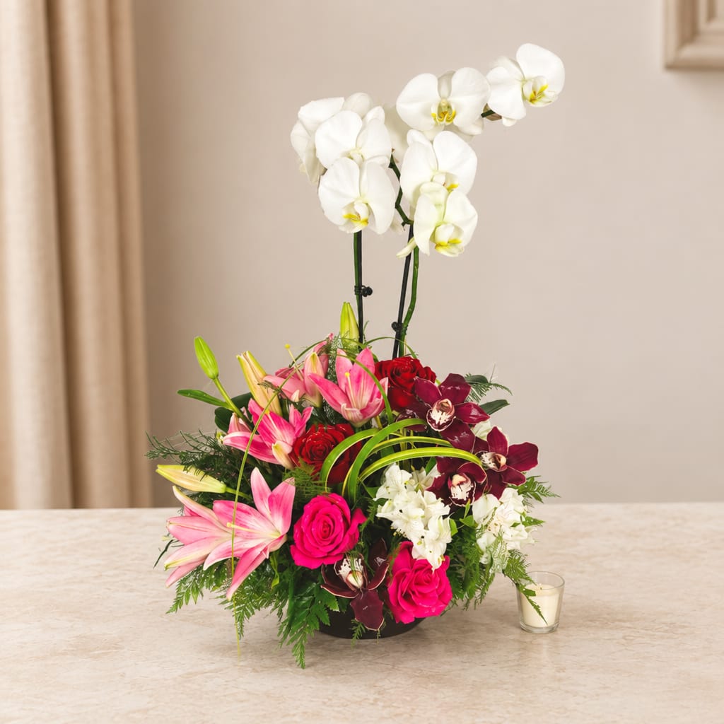 Mixed bouquet with white orchids, pink lilies, and red roses in a low container