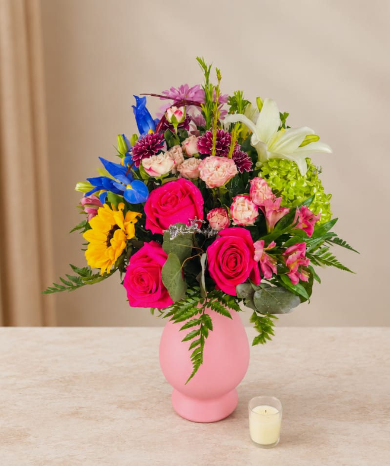 Colorful bouquet of mixed flowers in a pink vase with a small candle nearby