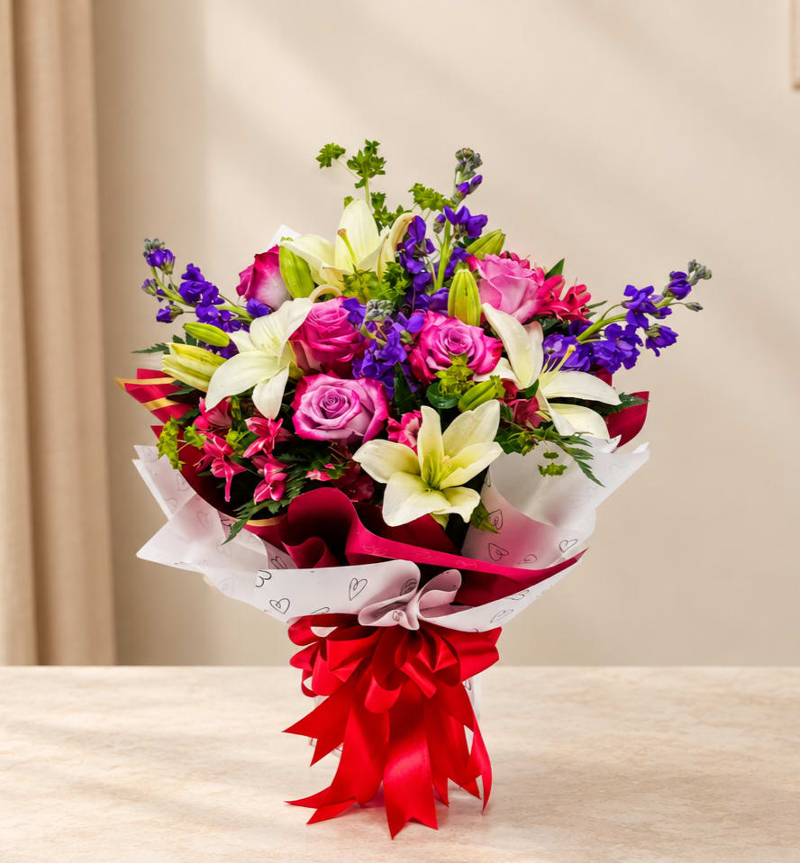 Bouquet of pink roses and white lilies wrapped with a red ribbon