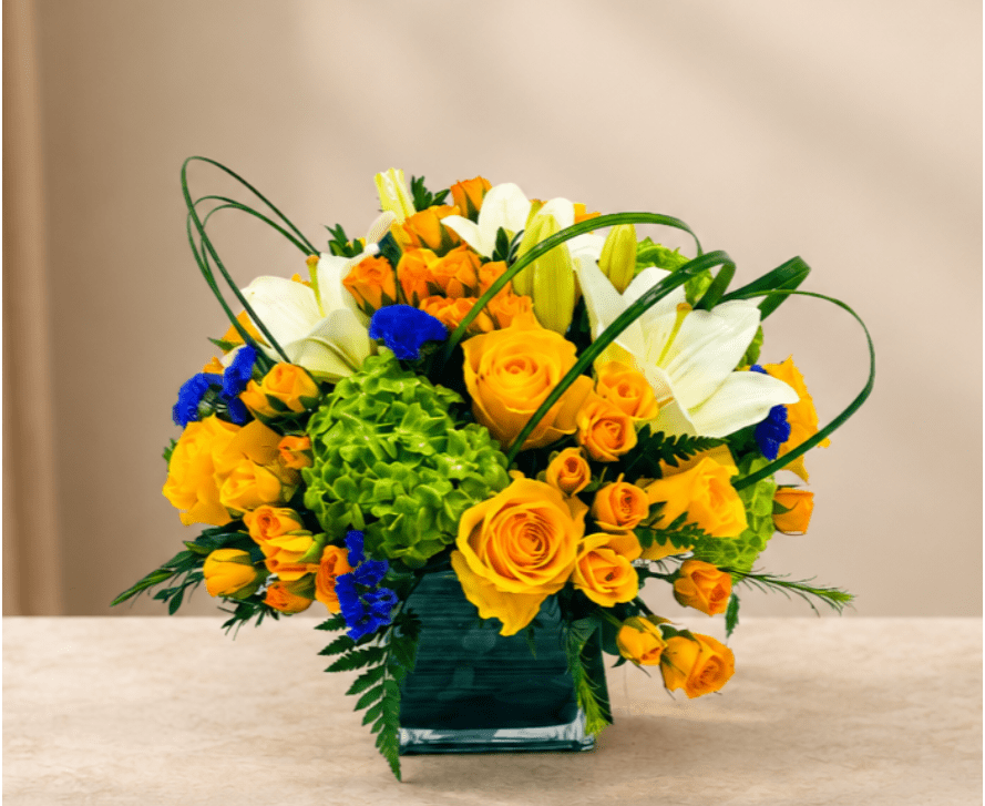 Yellow roses and white lilies in a square glass vase