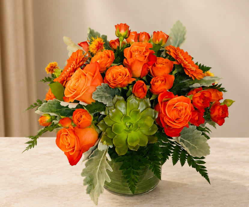 Orange roses and gerbera daisies in a glass vase with a green succulent accent