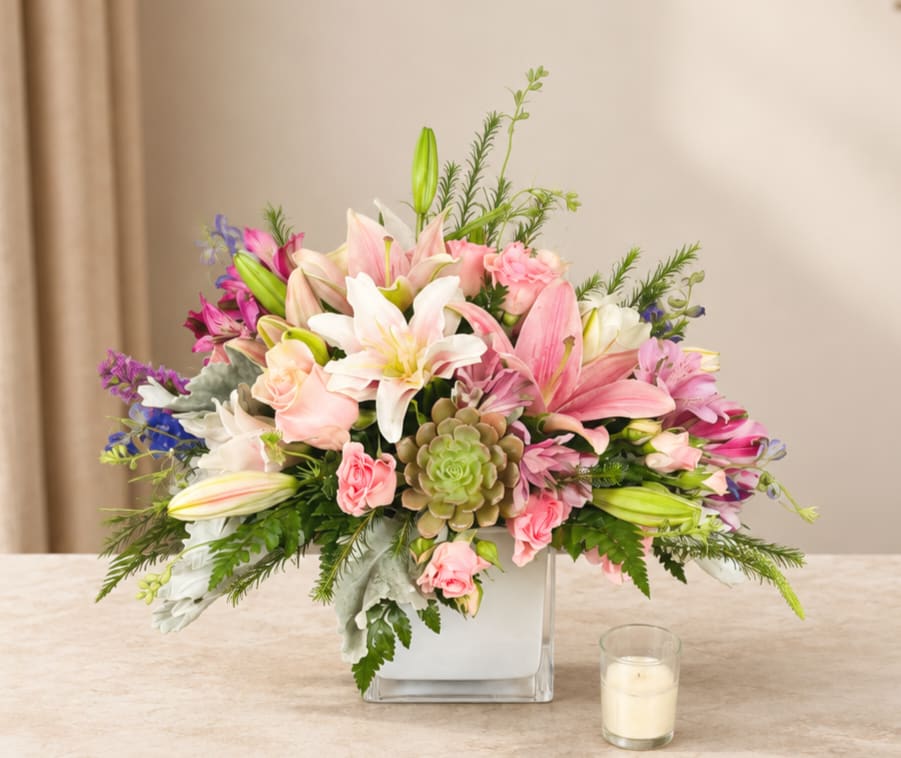 Pink and white lily bouquet in a square glass vase with a candle nearby