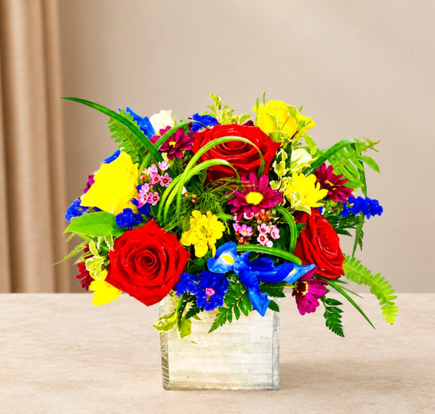 Bright mixed bouquet with red roses in a square glass vase