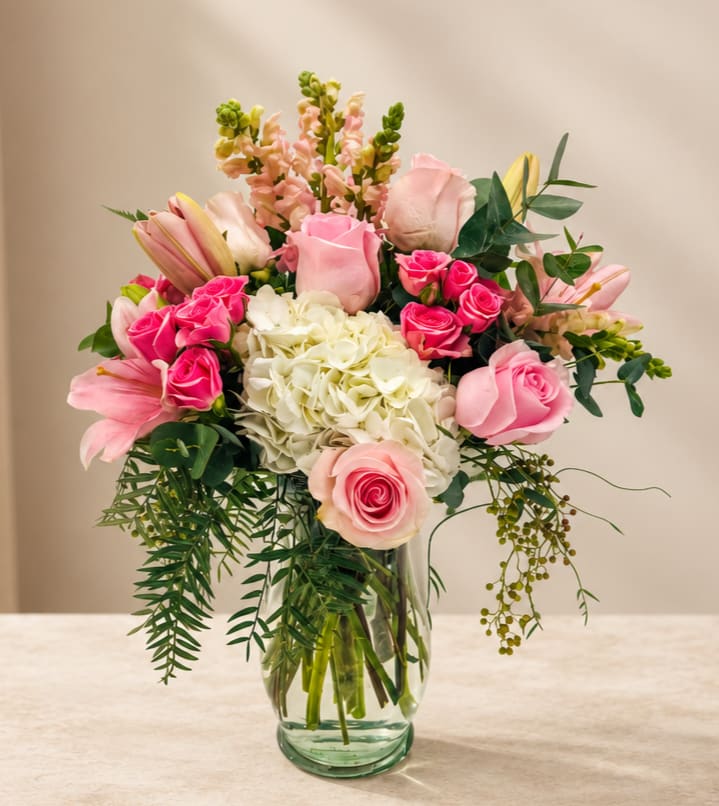 Pink roses and lilies arranged with white hydrangea in a glass vase